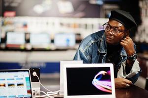 Stylish casual african american man at jeans jacket and black beret against new laptop screen at electronics store. photo