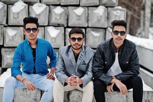 Group of three casual young indian mans in sunglasses posed against stone blocks. photo