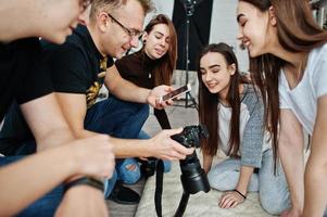 el equipo de fotógrafos que muestra imágenes en la pantalla de la cámara para las niñas modelos gemelas en el estudio. fotógrafo profesional en el trabajo. foto