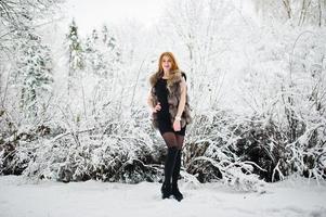 chica pelirroja con abrigo de piel caminando en el parque nevado de invierno. foto