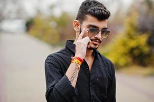 hombre con estilo indio en camisa negra y gafas de sol posó al aire libre. foto