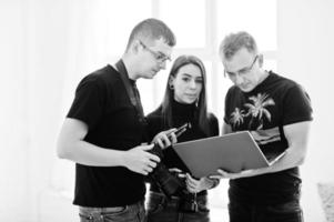 Photographer explaining about the shot to his team in the studio and looking on laptop. Talking to his assistants holding a camera during a photo shoot. Teamwork and brainstorm.