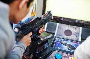 dos chicos asiáticos compiten en una máquina arcade de juegos de simulador de disparos. foto