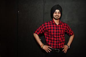 Indian man in checkered shirt and black turban against dark background. photo