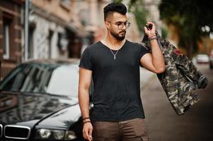 Awesome beautiful tall ararbian beard macho man in glasses and black t-shirt walking against business car. photo