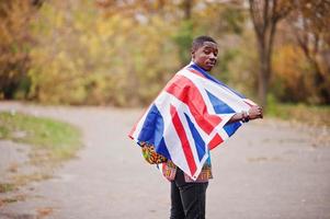 hombre africano en camisa tradicional de áfrica en el parque de otoño con bandera de gran bretaña. foto