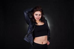 Studio portrait of sexy brunette girl in black leather jacket against black background. photo