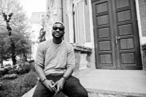 Elegante chico afroamericano con suéter gris y gafas de sol negras posadas en la calle. chico negro de moda. foto