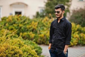 Indian stylish man at black shirt and sunglasses posed outdoor. photo