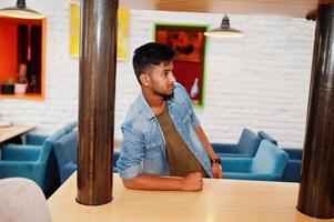 retrato de un guapo y exitoso surasiático barbudo, un joven autónomo indio con pantalones de mezclilla de pie en un café. foto