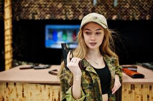 Military girl in camouflage uniform with gun at hand against army background on shooting range. photo