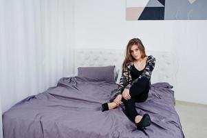 Handsome brunette girl wear military shirt, posing on bed at studio. Studio model portrait. photo