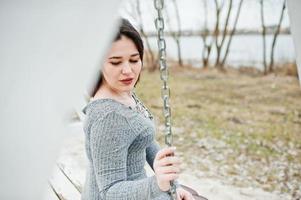 Portrait of brunette girl in gray dress sitting at white wooden construction. photo