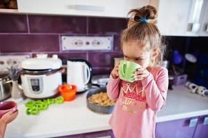 chica bebe compota en la cocina, momentos felices de los niños. foto