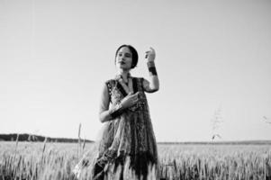 tierna niña india en sari, con maquillaje de labios violetas posada en el campo al atardecer. modelo indio de moda. foto