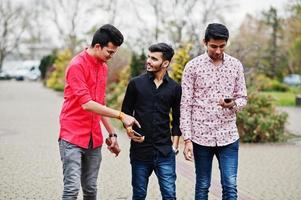 Three indian guys students friends walking on street and looking at mobile phone. photo
