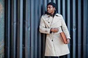 Handsome african american man posing outside in black hat and beige coat with folder in hand. photo