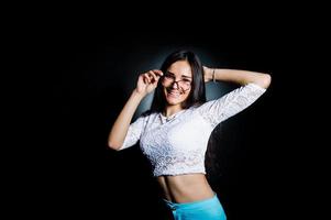 Portrait of an attractive young woman in white top and blue pants posing with her glasses in the dark. photo