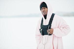 Stylish urban style african american man in pink hoodie posed at frozen lake in winter. photo