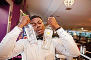 African american bartender at bar with two bottles. Alcoholic beverage preparation. photo