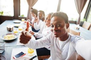 Happy african friends sitting, chatting in cafe and eat food. Group of black peoples meeting in restaurant and have dinner and make selfie. photo