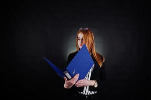 retrato de una mujer de negocios pelirroja con blusa a rayas, gafas y una chaqueta con una carpeta azul. foto