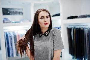hermosa chica morena en la boutique de la tienda de ropa en vestido gris. foto