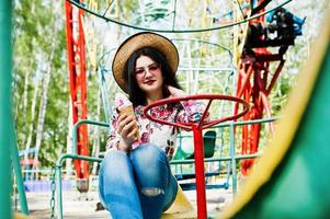 Portrait of brunette girl in pink glasses and hat with ice cream at amusement park.