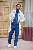 African american doctor male at lab coat with stethoscope outdoor against clinic door. photo