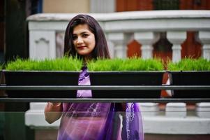 Indian hindu girl at traditional violet saree posed at  street against green grass on pots. Eco concept. photo