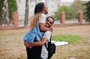 Two african students with backpack on yard of university hugs and having fun together. photo