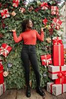 Portrait of a curly haired african woman wearing fashionable red turtleneck posing against christmas decorations, new year eve theme. photo