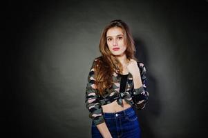 Handsome brunette girl wear military shirt and jeans, posing at studio against gray background. Studio model portrait. photo