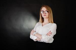 Studio portrait of blonde businesswoman in glasses, white blouse and black skirt against dark background. Successful woman and stylish girl concept. photo