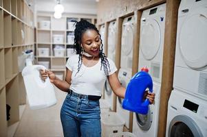 Cheerful african american woman hold detergent near washing machine in the self-service laundry. photo