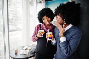 Two curly hair african american woman wear on sweaters with cups of tea posed at cafe indoor. photo