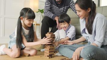 Fröhliche asiatische schöne thailändische Familienaktivität, Eltern, Vater, Mutter und Kinder haben Spaß beim Spielen und fröhliche Holzspielzeugblöcke zusammen auf dem Wohnzimmerboden, Freizeitwochenende und häuslichem Wohlbefinden. video