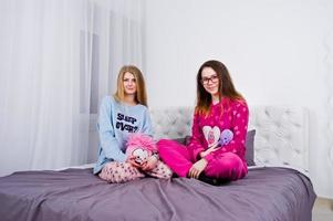 Two friends girls in pajamas having fun on bed at room. photo