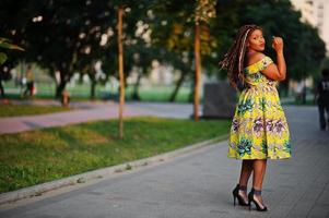 Cute small height african american girl with dreadlocks, wear at coloured yellow dress, posed at sunset. photo