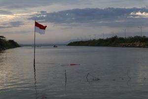 Indonesian flag fluttering against the background of the lake and the sky in the afternoon photo