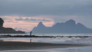 silhouet van een jonge fotograaf die foto's maakt tijdens een geweldige zonsopgang op het strand. video