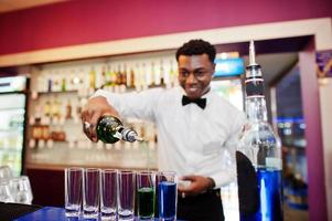 African american bartender at bar making coctails on shots. Alcoholic beverage preparation. photo