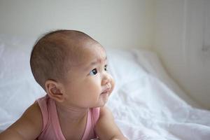 Asian cute baby in white sunny bedroom. Newborn child relaxing on bed photo