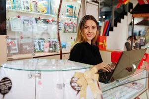 Portrait of young caucasian female woman seller using laptop. Small business of candy souvenirs shop. photo