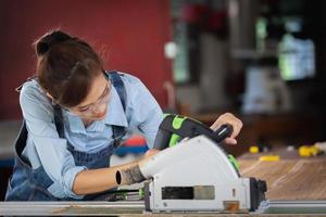 woman works in a carpentry shop. Attractive female carpenter using some power tools for her work in a woodshop.