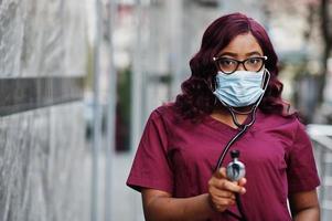 doctora afroamericana en uniforme de laboratorio rojo con máscara facial protectora. concepto de medicina, profesión y atención médica. detener la infección por coronavirus. foto