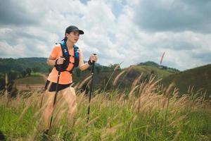 Young women active trail running across a meadow on a grassy trail high in the mountains in the afternoon with trekking pole photo