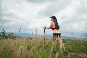 Young women active trail running across a meadow on a grassy trail high in the mountains in the afternoon with trekking pole photo