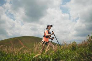 Young women active trail running across a meadow on a grassy trail high in the mountains in the afternoon with trekking pole photo