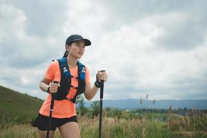 Young women active trail running across a meadow on a grassy trail high in the mountains in the afternoon with trekking pole photo